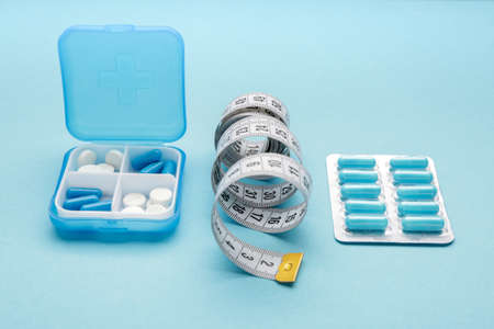 Box with weight loss pills and measuring tape on color backgroundの写真素材