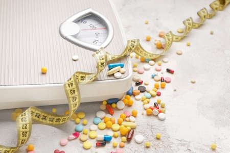 Weight loss pills, scales and measuring tape on gray backgroundの写真素材