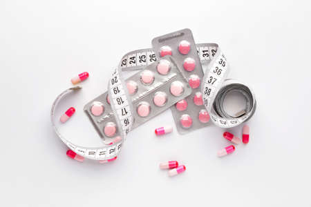 Weight loss pills with measuring tape on white backgroundの写真素材