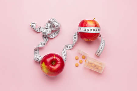 Bottle with weight loss pills, apples and measuring tape on color backgroundの写真素材