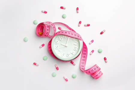 Alarm clock with weight loss pills and measuring tape on white backgroundの写真素材