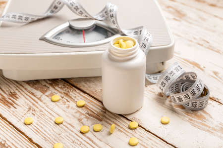 Bottle with weight loss pills, scales and measuring tape on white wooden backgroundの写真素材