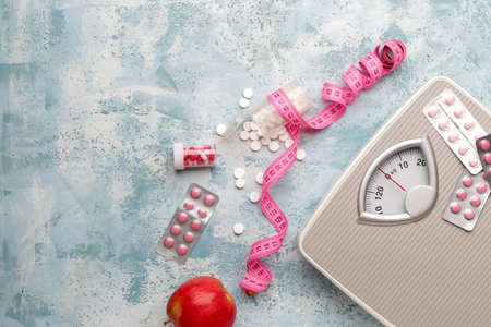 Weight loss pills with scales, apple and measuring tape on color backgroundの写真素材