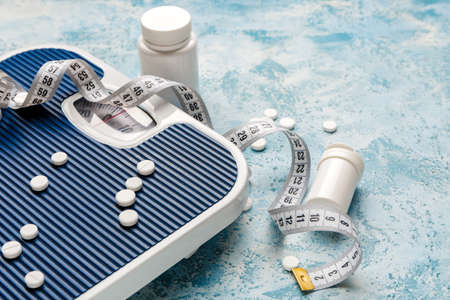 Bottles with weight loss pills, scales and measuring tape on color backgroundの写真素材