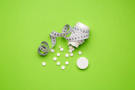 Bottle with weight loss pills and measuring tape on color backgroundの写真素材