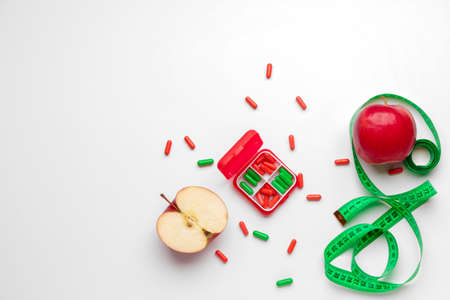 Box with weight loss pills, apples and measuring tape on white backgroundの写真素材