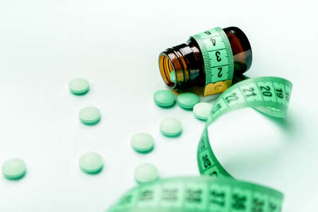 Bottle with weight loss pills and measuring tape on color backgroundの写真素材