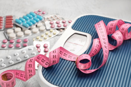 Weight loss pills, scales and measuring tape on gray backgroundの写真素材
