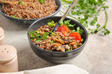 Bowl of tasty buckwheat porridge, tomatoes and mushrooms on tableの写真素材