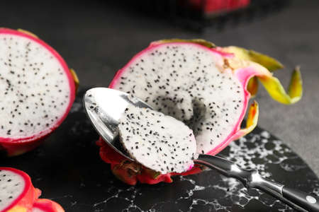 Board with tasty dragon fruit and spoon on dark background, closeupの写真素材