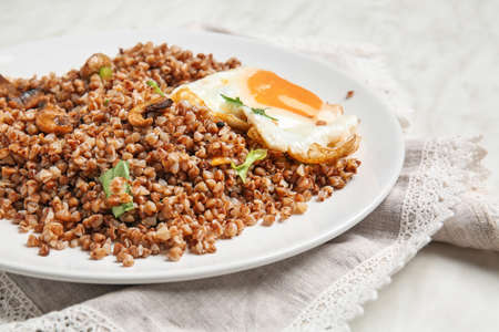 Plate with tasty buckwheat porridge, egg and mushrooms on tableの写真素材