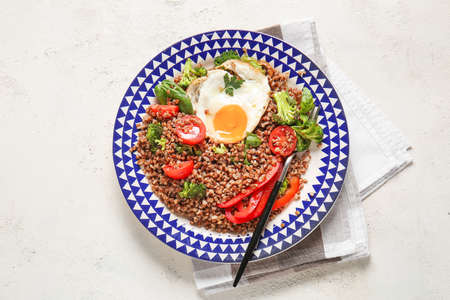 Plate with tasty buckwheat porridge, egg and vegetables on white backgroundの写真素材
