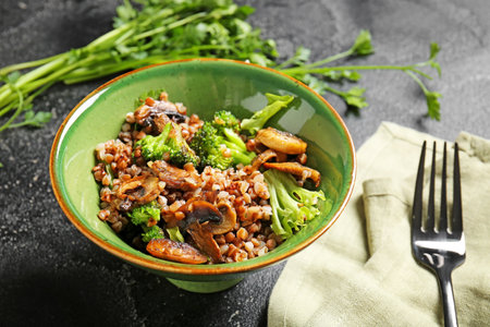 Bowl of tasty buckwheat porridge mushrooms and broccoli on dark backgroundの写真素材