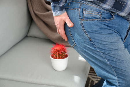 Elderly man near sofa with cactus at home. Hemorrhoids conceptの写真素材