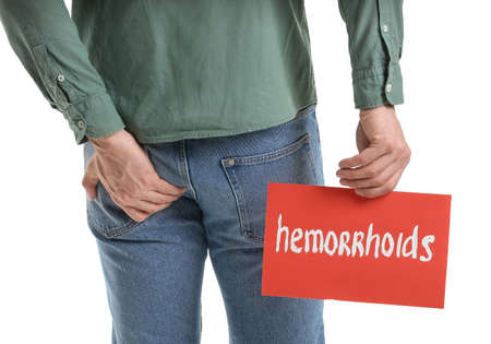 Young man holding paper with text HEMORRHOIDS on white backgroundの写真素材
