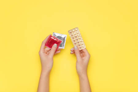 Female hands with contraceptive pills and condoms on color backgroundの写真素材