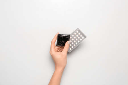 Female hand with contraceptive pills and condom on white backgroundの写真素材