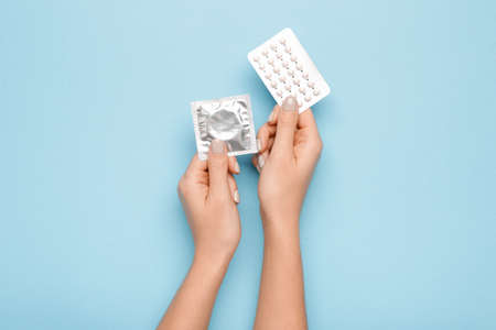 Female hands with contraceptive pills and condom on color backgroundの写真素材