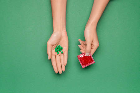Female hands with contraceptive pills and condom on color background
