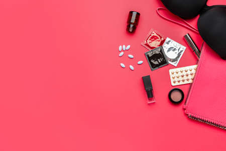 Female bag with contraceptive pills, condoms and bra on color background