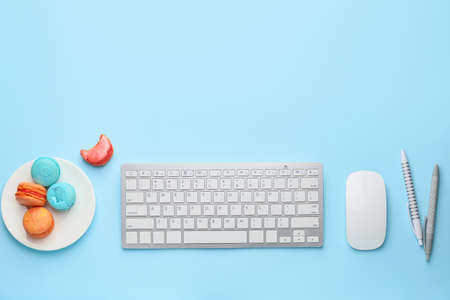 Stationery and computer keyboard with tasty macarons on color backgroundの写真素材