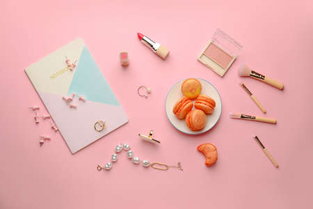 Makeup cosmetics and accessories with tasty macarons on color background
