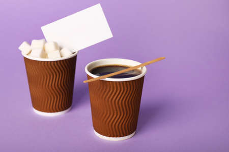 Takeaway cups of coffee with sugar business card on color backgroundの写真素材