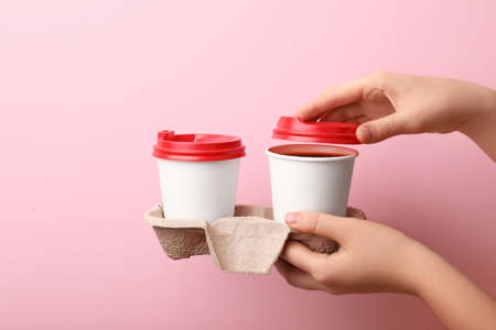 Female hands with takeaway cups of coffee on color backgroundの写真素材