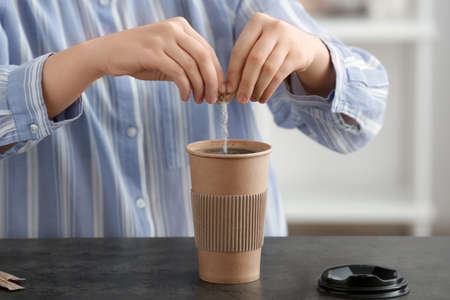 Woman with adding sugar to coffee in cup on tableの写真素材