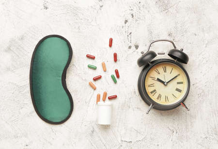 Sleep mask, pills and alarm clock on light backgroundの写真素材