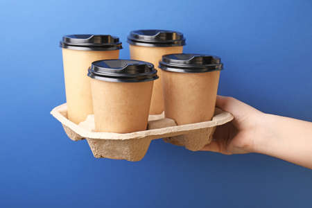 Female hand with takeaway coffee cups on color backgroundの写真素材