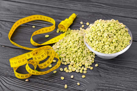 Bowl with green coffee beans and measuring tape on tableの写真素材