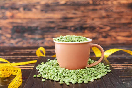 Cup with green coffee beans and measuring tape on tableの写真素材