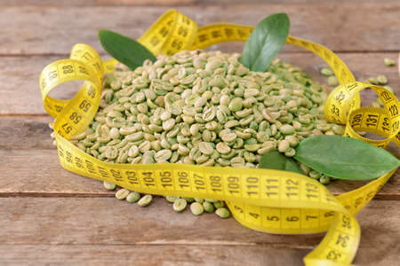 Green coffee beans and measuring tape on tableの写真素材