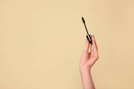 Female hand with mascara on color backgroundの写真素材