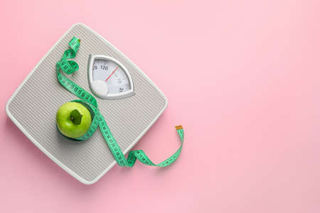Weight scales with measuring tape and apple on color background. Slimming conceptの写真素材