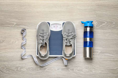 Weight scales with measuring tape, sport shoes and bottle of water on wooden background. Slimming conceptの写真素材
