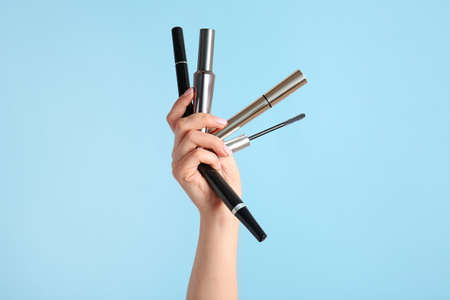 Female hand with mascara on color background