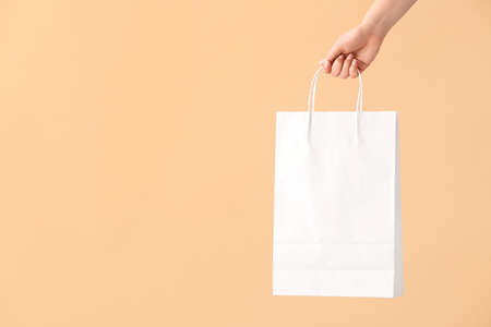Female hand with paper shopping bag on color backgroundの写真素材