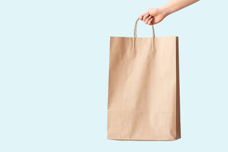 Female hand with paper shopping bag on color backgroundの写真素材