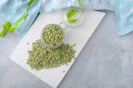 Jar with green coffee beans and measuring tape on color backgroundの写真素材