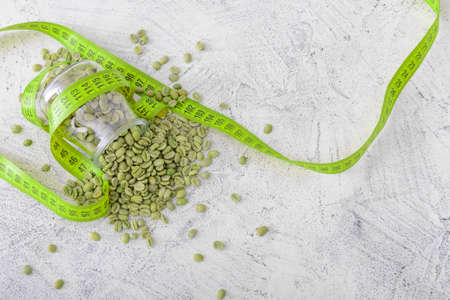 Jar with green coffee beans and measuring tape on white background