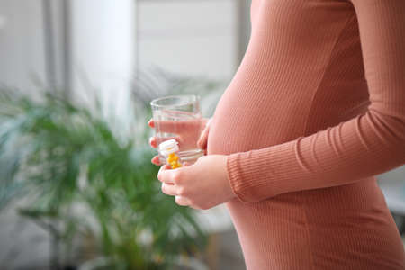 Young pregnant woman with medicine at homeの写真素材