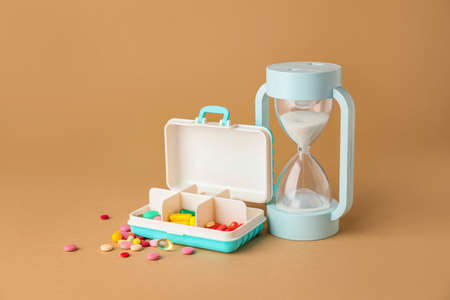 Box with different pills and hourglass on color backgroundの写真素材
