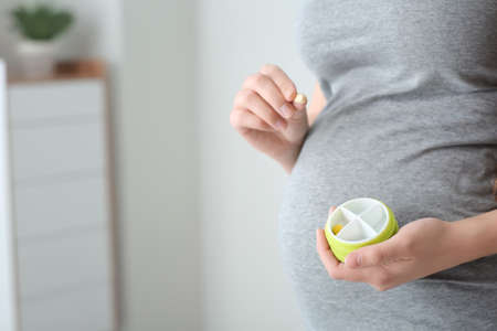 Young pregnant woman with pills box at home, closeupの写真素材
