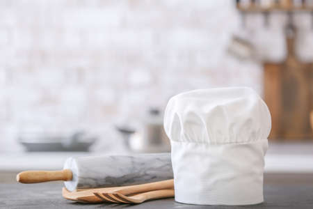 Chef's hat and utensils on table in kitchenの写真素材