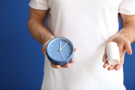 Young man with sleeping pills and clock on color background, closeupの写真素材
