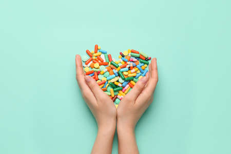 Female hands and heart made of pills on color background