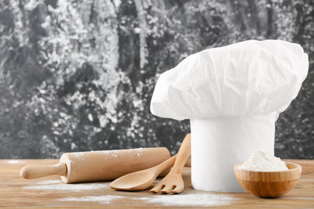 Chef's hat and kitchenware on table against grunge backgroundの写真素材