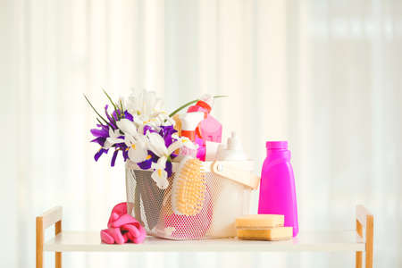Set of cleaning supplies and spring flowers on table in roomの写真素材